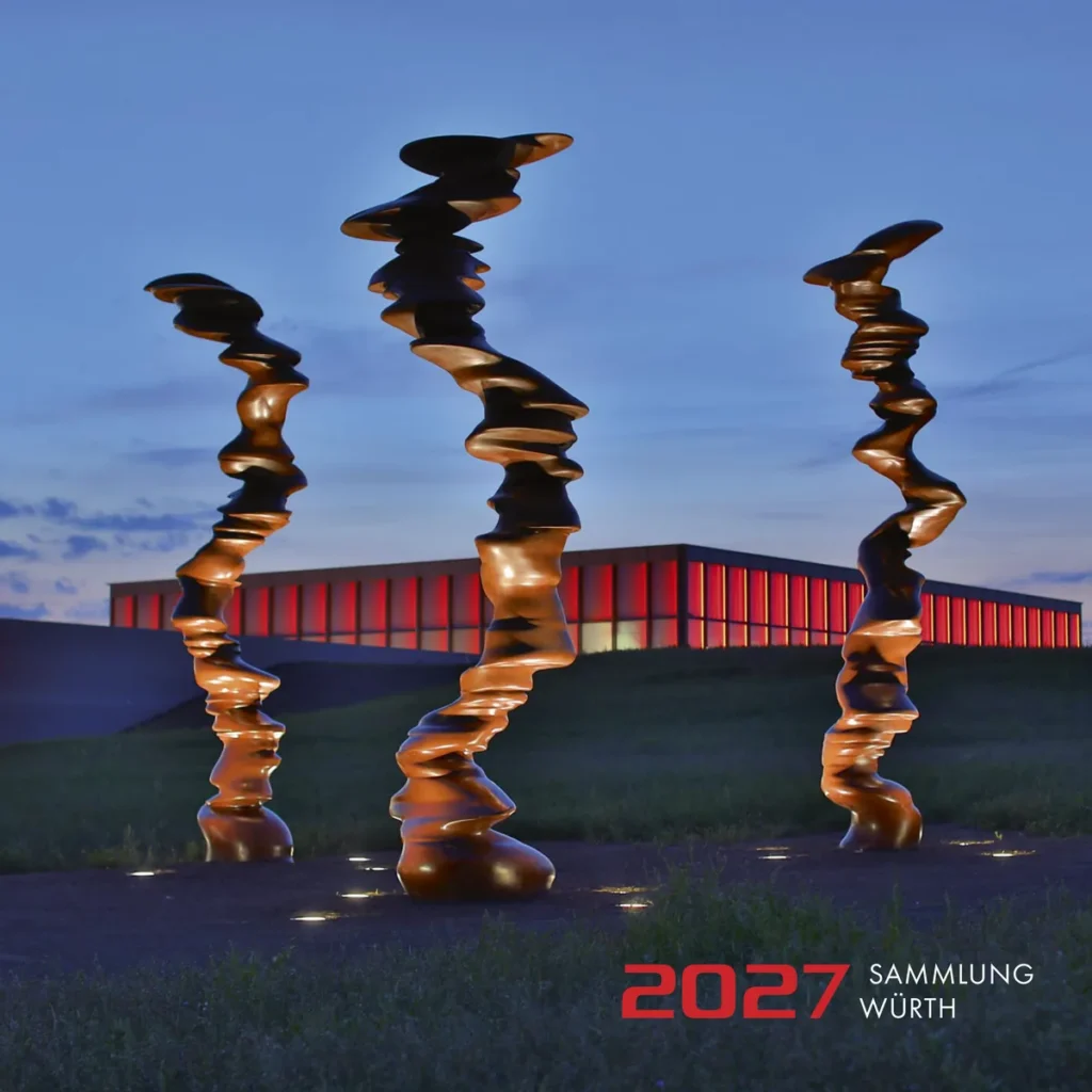 Kunstkalender 2027 Sammlung Würth, Titelblatt: drei hohe Bronzeskulpturen in der Abenddämmerung vor einem rot beleuchteten Museumsbau